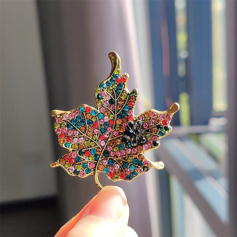 Multicoloured rhinestone leaf brooch on a plain background