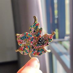 Multicoloured rhinestone leaf brooch on a plain background
